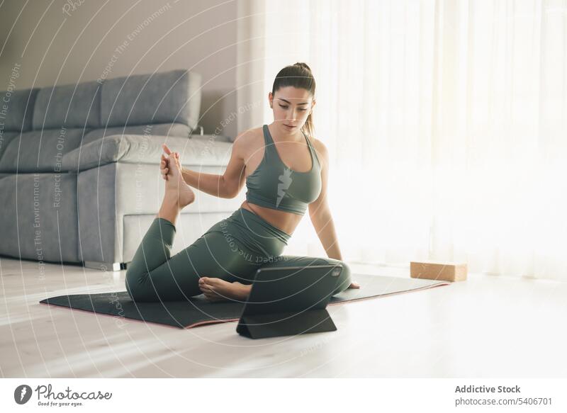 Fitte Frau, die während einer Online-Stunde zu Hause eine Yoga-Pose einnimmt Sportlerin Dehnung online benutzend Tablette beweglich üben Lektion Training Asana