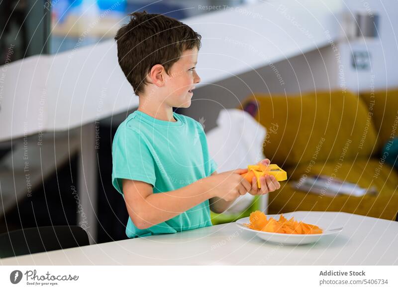 Kleiner Junge steht am Tisch mit frischer Karotte in der Küche Kind Scheibe Möhre Teller Hilfsbereitschaft Anspitzer beschäftigt heimwärts Kindheit Vitamin