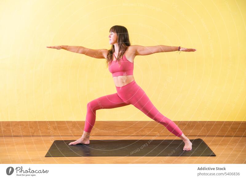Junge Frau macht Warrior II Yoga-Pose auf Matte in der Nähe der gelben Wand üben Dehnung virabhadrasana Unterlage Gleichgewicht Barfuß jung Sportbekleidung