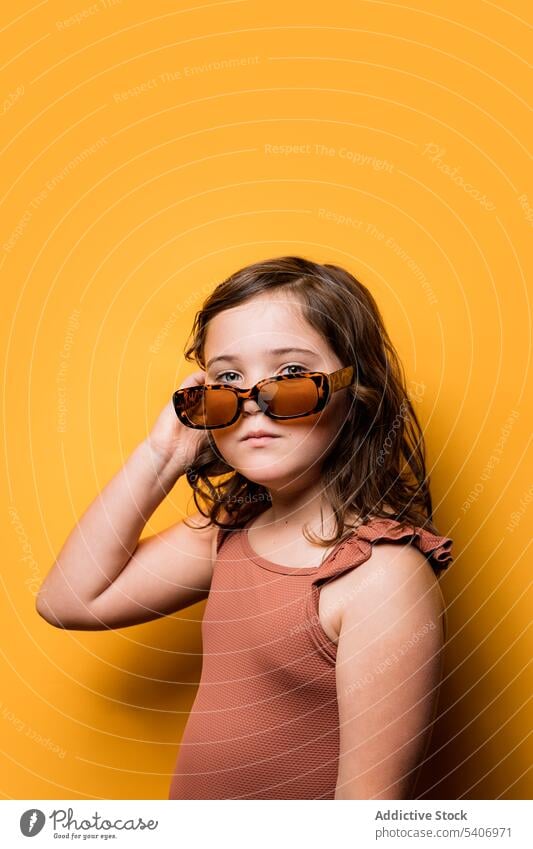 Niedliches kleines Mädchen mit Sonnenbrille, das sein Haar berührt und in die Kamera schaut Stil Haare berühren selbstbewusst Kind Sommer Feiertag cool Porträt
