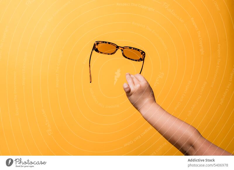 Anonymes Kind zeigt Sonnenbrille in gelbem Studio manifestieren Accessoire Stil Hand Mädchen Mode hell zeigen Arme Arm angehoben Kindheit Design trendy Feiertag