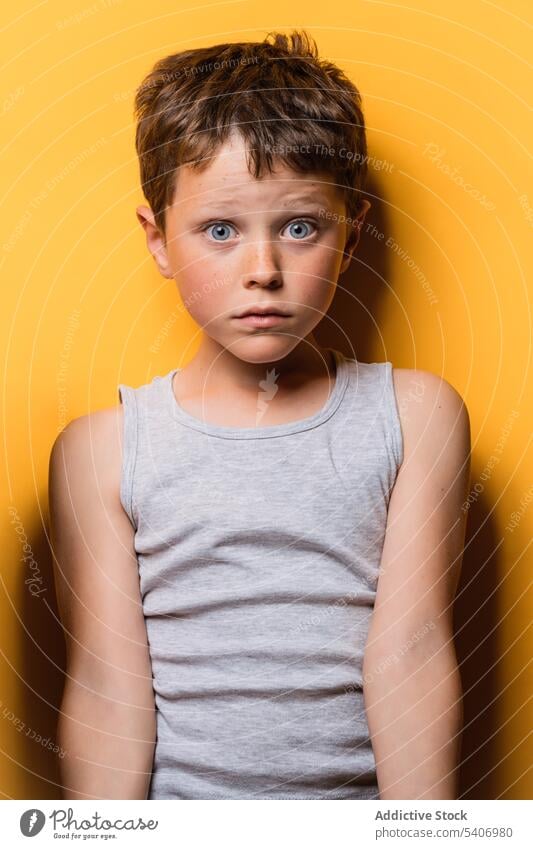 Schockiertes Kind, das mit Erstaunen in die Kamera schaut, in einem gelben Studio Junge Starrer Blick Überraschung expressiv wow erschrecken Porträt erstaunt