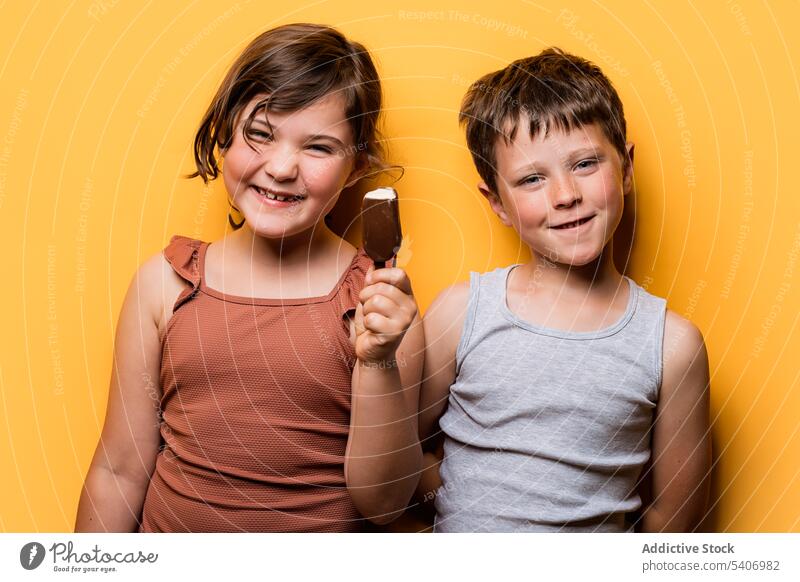 Glückliches Mädchen hält ein Eis in der Hand, während es mit einem Jungen im Studio steht Kinder Schokolade Speiseeis Bar Leckerbissen süß Sommer lustig