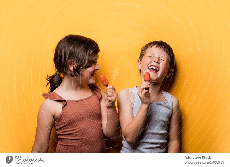 Fröhlicher Junge und Mädchen essen Eis im Studio Kinder Eispop Spaß haben Lachen Stieleis Kindheit Speiseeis lustig expressiv Humor Witz sorgenfrei Lächeln