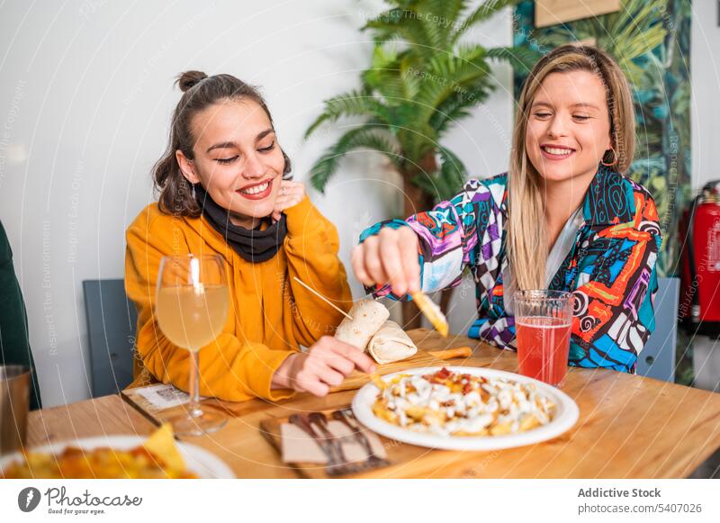 Fröhliche Freunde haben Spaß mit Getränken und Tellern voller Essen am Tisch Frauen essen Lebensmittel Lächeln positiv Snack Mahlzeit Esstisch lässig heiter