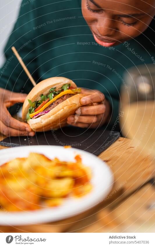 Afroamerikanische Frau isst leckeren Burger essen geschmackvoll Snack Restaurant Kantine Portion Lebensmittel Café jung hungrig Speise Teller Tisch Mahlzeit