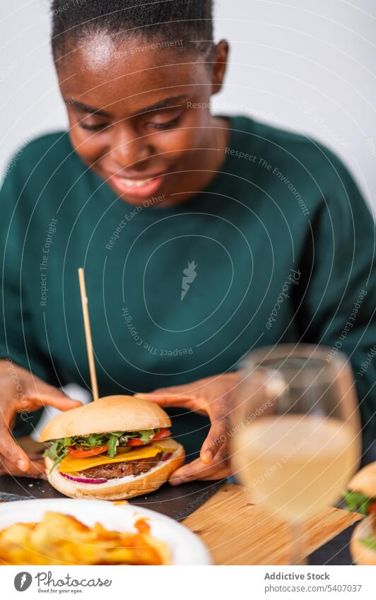 Lächelnde afroamerikanische Frau isst leckeren Burger essen geschmackvoll Snack Restaurant Kantine Portion Lebensmittel Café jung hungrig Speise Teller Tisch
