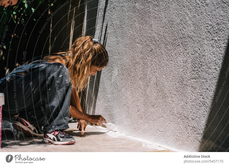 Junge Frau in Freizeitkleidung sitzt und malt Wand mit Pinsel im Tageslicht Farbe Stock Pinselblume renovieren Handarbeit heimwärts jung Hobby Prozess