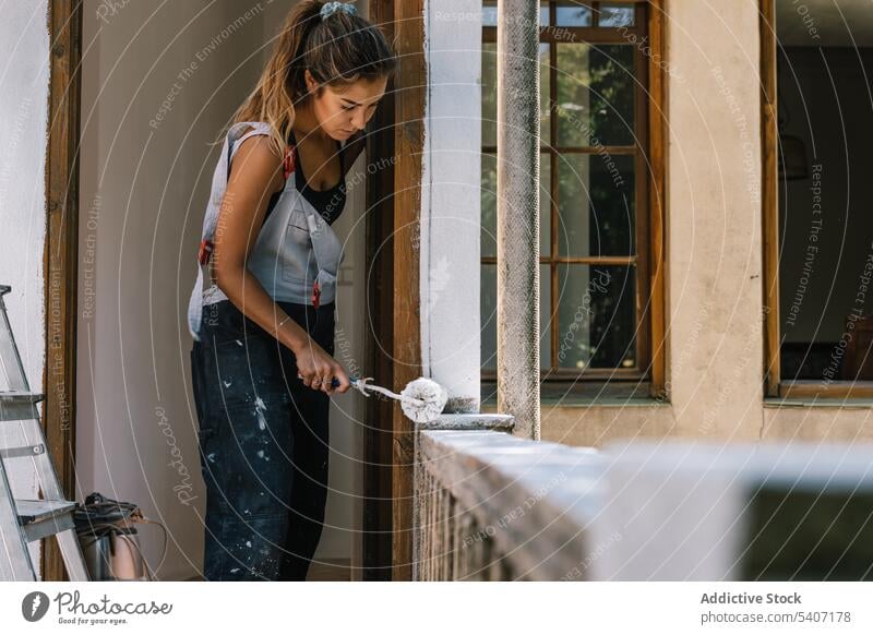 Fokussierte Frau malt auf dem Balkon mit einem Roller Farbe Anstreicher renovieren Zaun Haus Werkzeug verbessern hölzern lässig tagsüber heimwärts Appartement