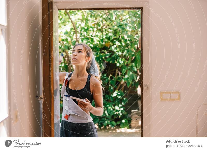 Junge Frau streicht tagsüber die Tür eines Hauses Farbe renovieren Türöffnung offen Arbeit wohnbedingt verbessern kreativ Eingang heimwärts lässig jung neu