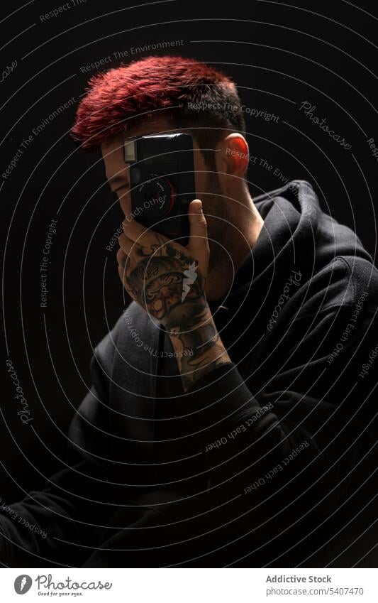 Junger anonymer Mann, der ein Foto mit der Kamera macht Fotoapparat Fotograf Porträt Tattoo schießen gefärbtes Haar fotografieren Atelier Linse Stil Fotokamera