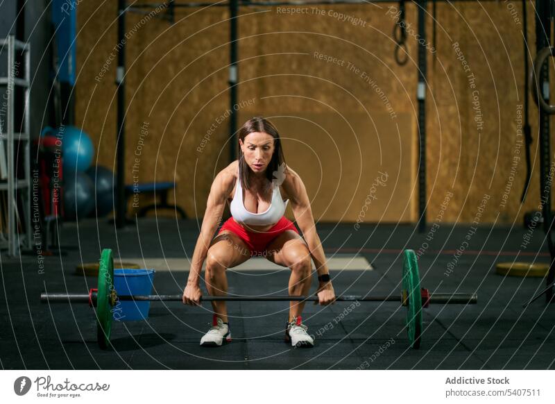Starke, konzentrierte Sportlerin hebt eine Langhantel im Fitnessstudio Kniebeuge Gewichtheben Overhead Curl-Hantel Übung schwer Frau reif Training Gesundheit