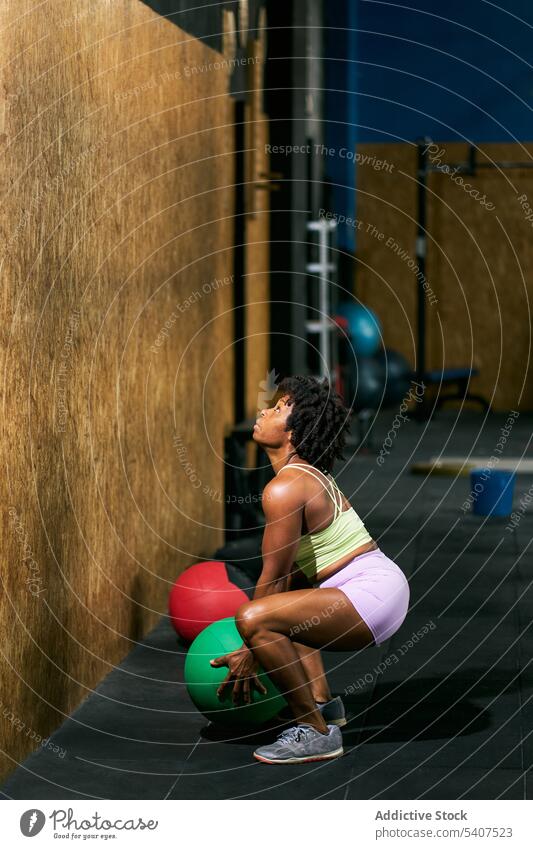 Starke schwarze Sportlerin wirft Medizinball gegen die Wand werfen Ball Übung Kraft Gewicht Training Fitnessstudio hocken Frau reif Afroamerikaner ethnisch