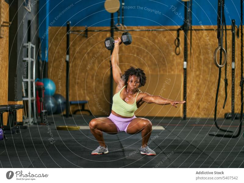 Schwarze Sportlerin in der Hocke mit schwerer Kurzhantel Kniebeuge Gewichtheben Übung anstrengen Training Fitnessstudio Frau reif Afroamerikaner schwarz