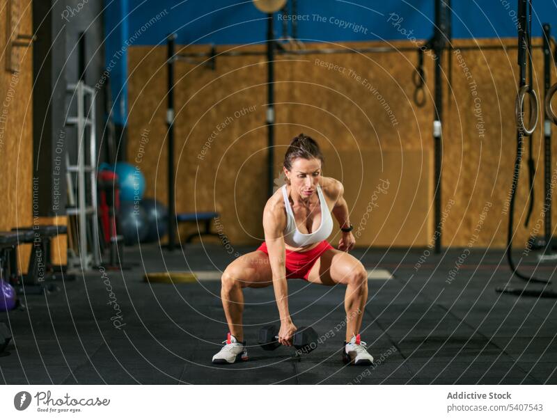 Sportlerin in der Hocke mit schwerer Kurzhantel Kniebeuge Gewichtheben Übung anstrengen Training Fitnessstudio Frau reif Gerät muskulös Sportbekleidung