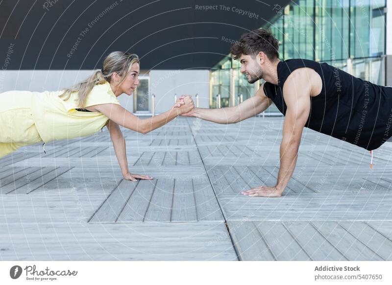 Selbstbewusstes Paar bei einer Plank-Übung, bei der die Hände an einem offenen Ort gehalten werden Training Händchenhalten Dehnung Partnerschaft Schiffsplanken