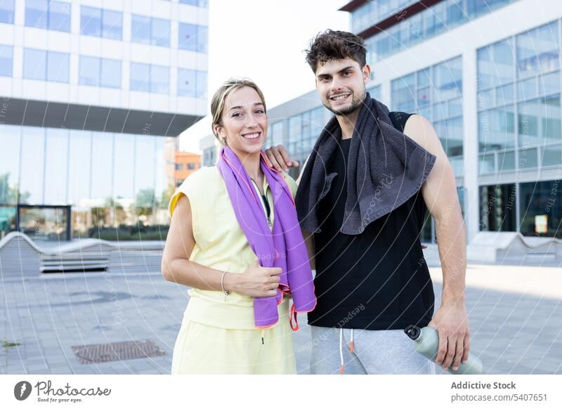 Glückliches junges Paar steht auf der Straße im Tageslicht in der Nähe von Glaswänden Gebäude Handtuch Flasche Hydrat Lächeln Großstadt Partnerschaft Liebe