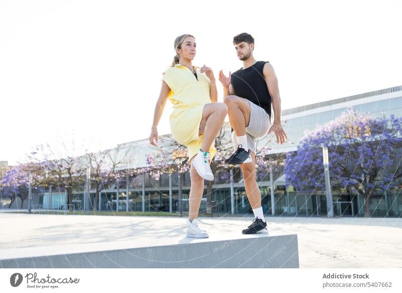 Stilvolles junges Paar macht Beinübungen auf der Straße springen Training Aufwärmen Übung Sportpark Bein hoch aktiv ernst sportlich Sportbekleidung Sportler