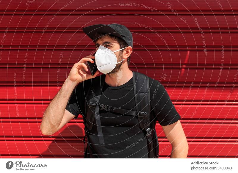 Mann in Maske spricht auf Smartphone auf rotem Hintergrund sprechen Mundschutz Bund 19 neue Normale Telefonanruf stylisch Bekleidung benutzend Apparatur Straße