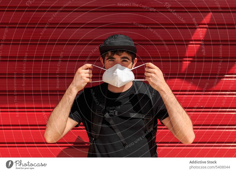 Anonymer Mann mit Maske in der Nähe der roten Mauer in der Stadt angezogen Mundschutz Atemwegserkrankungen COVID19 behüten neue Normale Selbstisolierung Wand