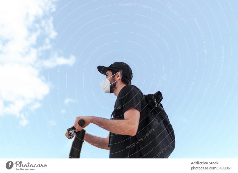 Unbekannter Mann mit Rucksack und Maske auf Motorroller unter freiem Himmel Laufwerk Tretroller Mundschutz Blauer Himmel Bund 19 wolkig modern Verkehr