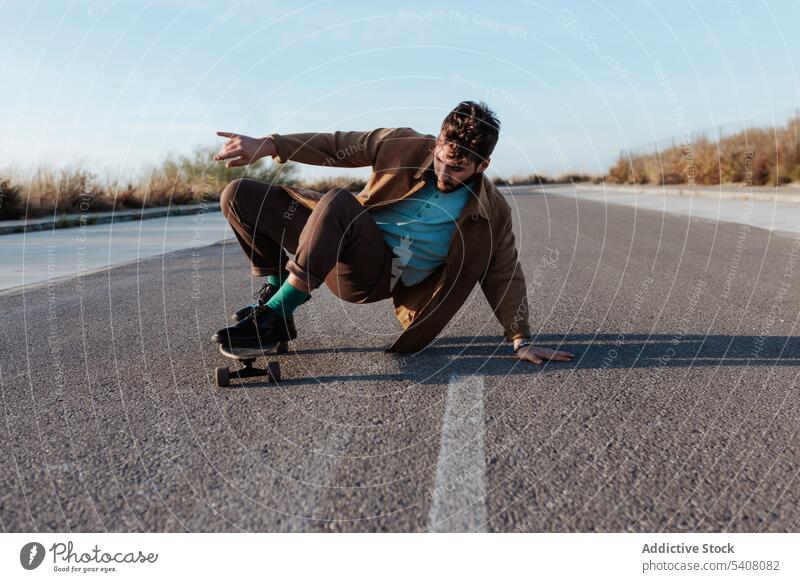 Trendiger Skater, der auf einer Landstraße einen Trick vorführt Mann ausführen Straße Landschaft Natur ländlich Asphalt berühren Boden Fähigkeit Talent männlich