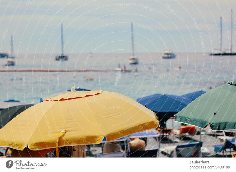 Sonnenschirme in gelb, blau und grün, dahinter das Meer, an der Küste der italienischen Riviera Ligurien Stand Wasser Boote Baden Sonnenbad Urlaub sonnig schön