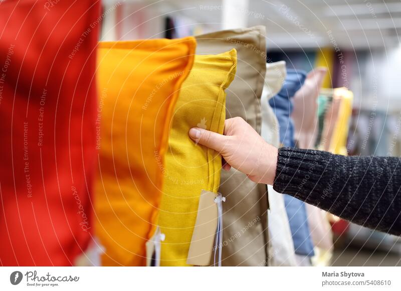 Mann wählt Kissen im Geschäft aus. Eine Vielzahl von farbigen Kissen auf einem Einkaufsstand im Supermarkt Wahl Kopfkissen Werkstatt Laden Varieté Hand