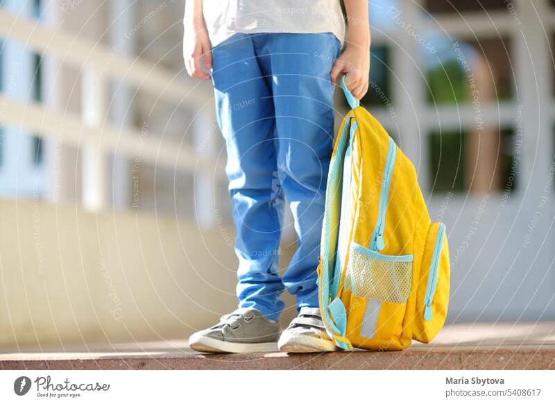 Kleiner Schüler mit einem Rucksack auf den Stufen der Treppe des Schulgebäudes. Nahaufnahme des Kindes Beine, Hände und Schultasche des Jungen auf der Treppe des Schulhauses stehend.back to school Konzept.
