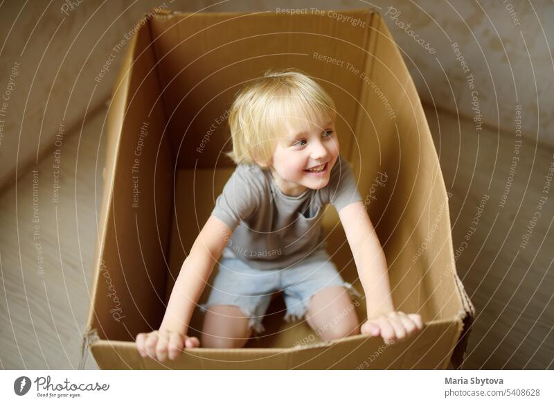 Niedlicher Vorschuljunge spielt in einem Karton während des Umzugs der Familie in ein neues Haus. Kinder spielen ist ein Weg zur Entwicklung kreativer Fähigkeiten.