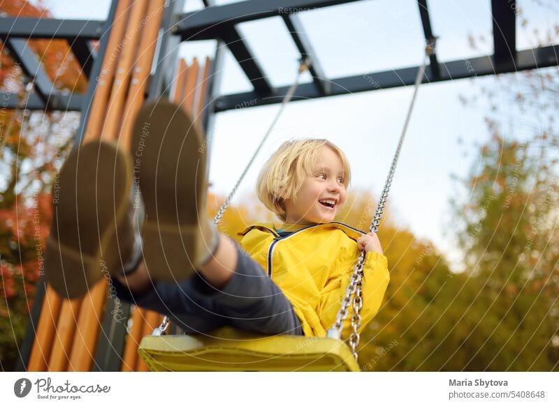 Kleiner Junge hat Spaß auf einer Schaukel auf dem Spielplatz im öffentlichen Park am Herbsttag. Glückliches Kind genießen schwingen. Aktiv im Freien Freizeit für Kind