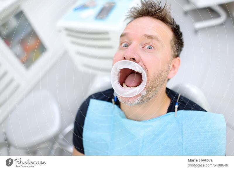 Verängstigter Patient auf dem Stuhl in der Zahnklinik. Kieferorthopädischer und prothetischer Termin. Angst vor Zahnärzten Konzept. Zahnarzt Leckerbissen Zähne