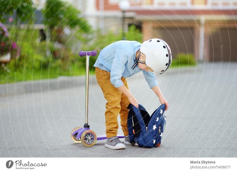 Kleiner Junge mit Schutzhelm fährt mit dem Roller zur Schule. Qualität schützen Ausrüstung für Sicherheit Kinder auf der Straße der Stadt. Zurück zu Schule Konzept.