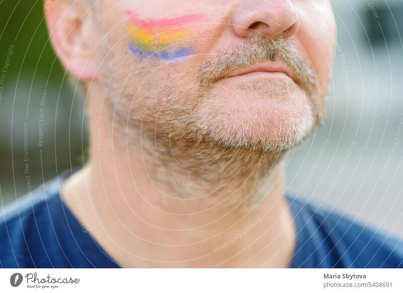 Nahaufnahme von Gesicht Mann Aktivist mit Malerei Regenbogen auf der Wange während LGBT Pride Event. Kämpfen für die Gleichheit der Rechte von sexuellen Minderheiten.