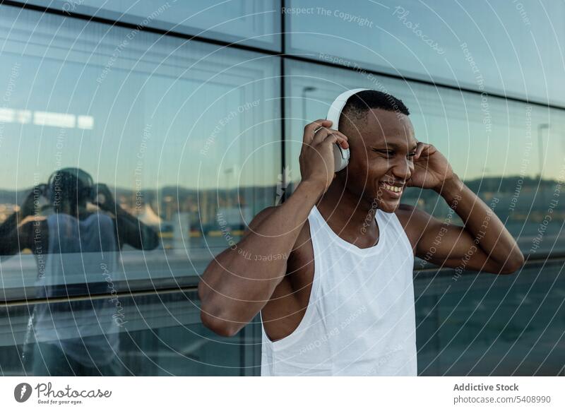Fröhlicher schwarzer Mann, der mit Kopfhörern Musik hört heiter zuhören Freude Klang Athlet Drahtlos Optimist männlich Training Gerät Apparatur Lächeln Melodie