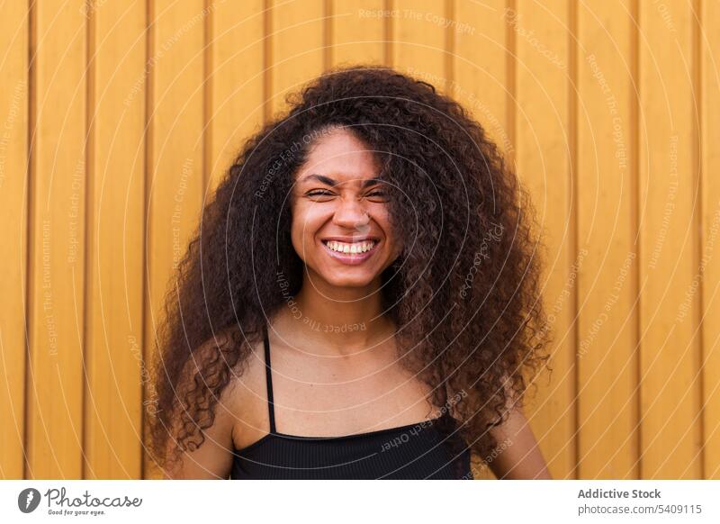 Fröhliche schwarze Frau mit lockigem Haar auf der Straße krause Haare Afro-Look Frisur Lächeln Porträt herzlich offen jung ethnisch Afroamerikaner Freude