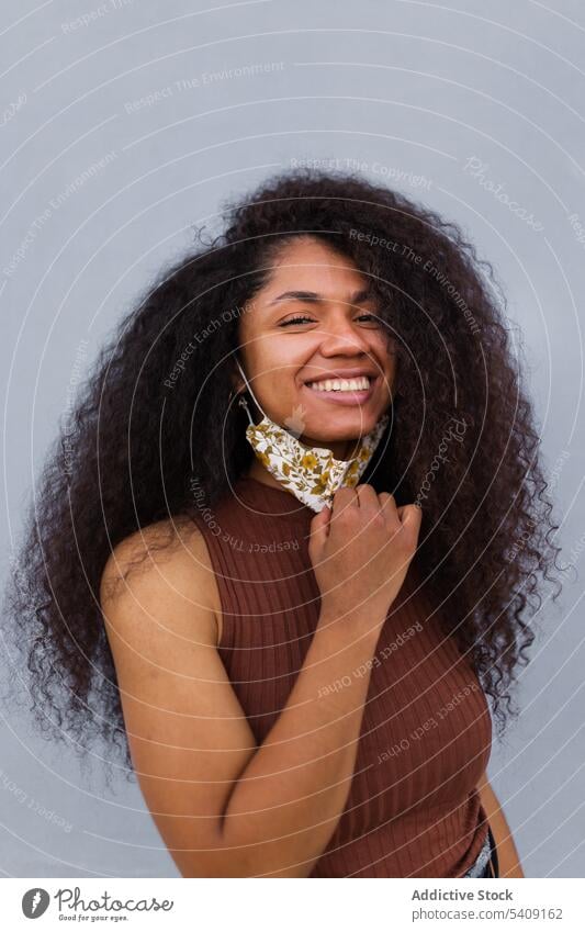 Lächelnde schwarze Frau mit Maske auf der Straße Coronavirus Pandemie Mundschutz neue Normale Großstadt behüten verhindern ethnisch Afroamerikaner krause Haare