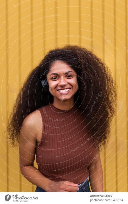 Erfreute schwarze Frau genießt Musik in Kopfhörern krause Haare Afro-Look Frisur charmant Lächeln natürlich Schönheit Straße zuhören ethnisch Afroamerikaner