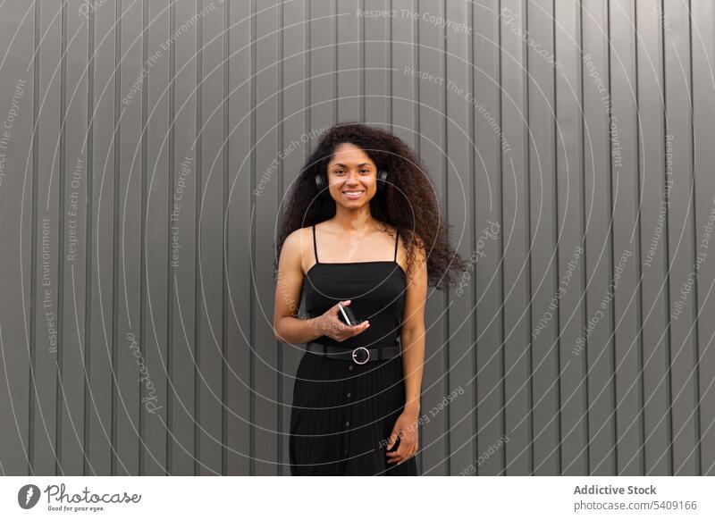 Optimistische schwarze Frau, die auf der Straße Musik hört zuhören Kopfhörer meloman genießen Afro-Look Browsen Smartphone Frisur krause Haare ethnisch