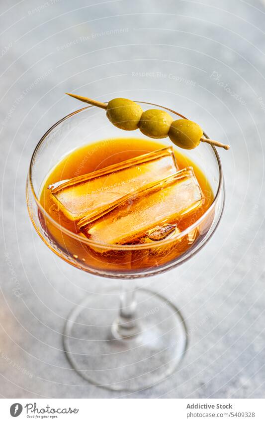 Glas Cocktail mit alkoholischem Whiskey und Olivenstäbchen Eis trinken Alkohol Glaswaren Scheibe kleben oliv Portion Aperitif dienen Getränk lecker köstlich