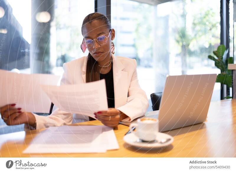 Konzentrierte Frau erledigt Papierkram im Büro Geschäftsfrau Konzentration Fokus Schriftstück lesen Laptop Arbeit Kaffee beschäftigt Unternehmer Tisch