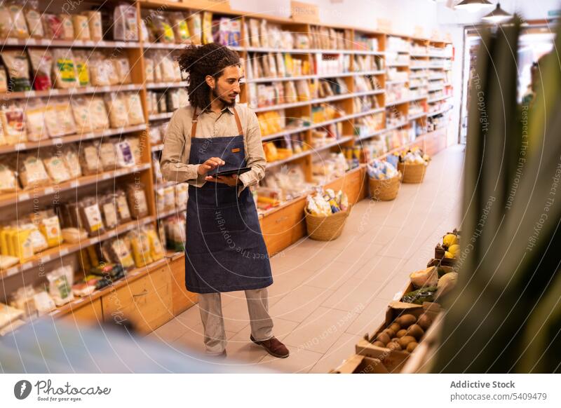 Seriöser Mann mit Tablette bei der Warenkontrolle im Lebensmittelladen Werkstatt Supermarkt Bestandsaufnahme Kontrolle prüfen Lebensmittelgeschäft ernst