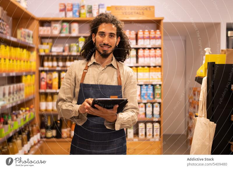 Zufriedener Mann mit Tablet, der im Lebensmittelgeschäft seine Waren kontrolliert Werkstatt Tablette Supermarkt Bestandsaufnahme Kontrolle prüfen Lächeln
