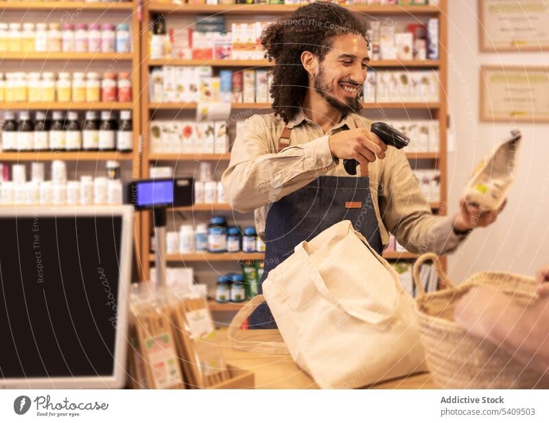 Lächelnder ethnischer männlicher Verkäufer beim Scannen von Produkten am Kassenschalter Mann Kassierer umweltfreundlich verkaufen heiter Lebensmittelgeschäft