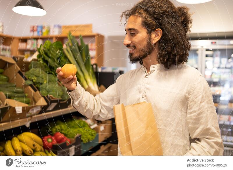 Glücklicher Mann wählt Obst im Laden am Gemüseregal aus Werkstatt Tüte Lebensmittelgeschäft Kunde Supermarkt Käufer Regal Porträt Ware männlich jung kaufen