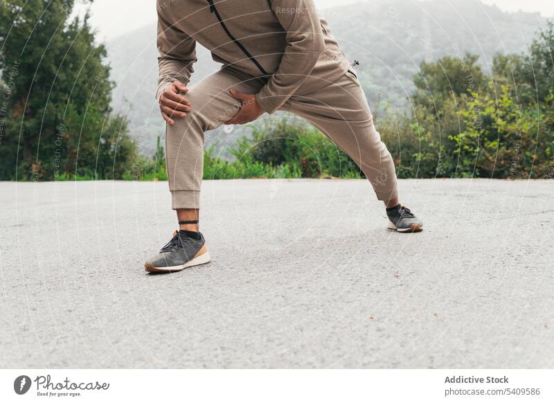 Unbekannter Mann in Turnschuhen, der sein Bein ausstreckt und eine Übung auf der Straße macht Aufwärmen Dehnung Training Fitness Sommer männlich Sportbekleidung