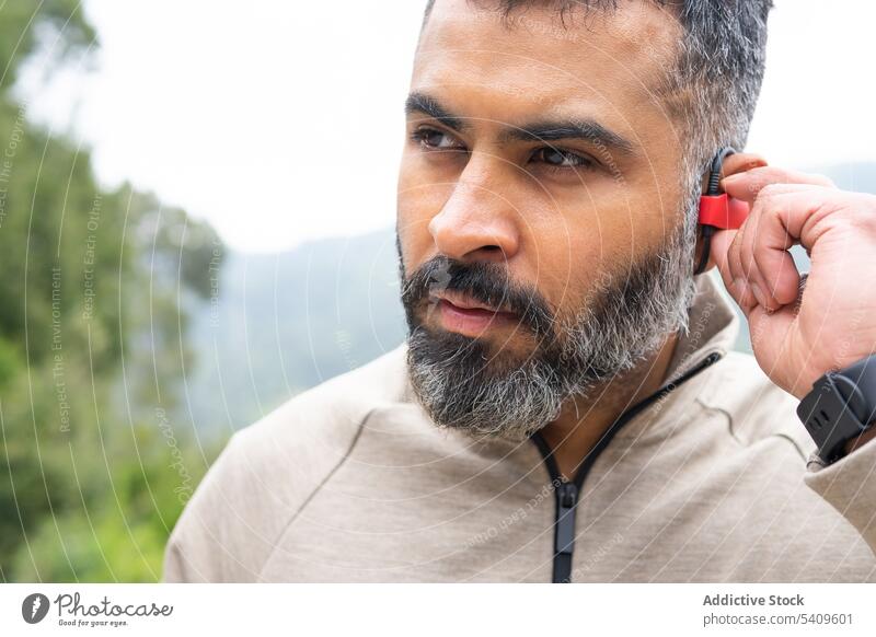 Mann in Sportkleidung beim Einschalten eines kabellosen Kopfhörers Lebensstile Vitalität zuhören Marathon Wohlbefinden Ethnizität Jogger Joggen Läufer