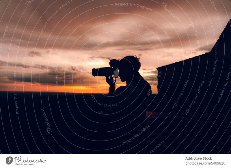 Unbekannter Mann mit Kamera, der den orangefarbenen Abendhimmel mit schwarzen Wolken fotografiert fotografieren Fotokamera Sonnenuntergang Himmel Natur Cloud