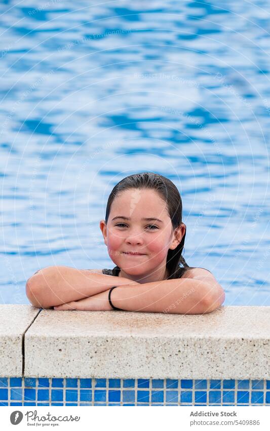 Glückliches Kind am Swimmingpool im Tageslicht stehend Lächeln Pool nasses Haar Wasser genießen froh die Hände gekreuzt Beckenrand Mädchen Sommerzeit Urlaub