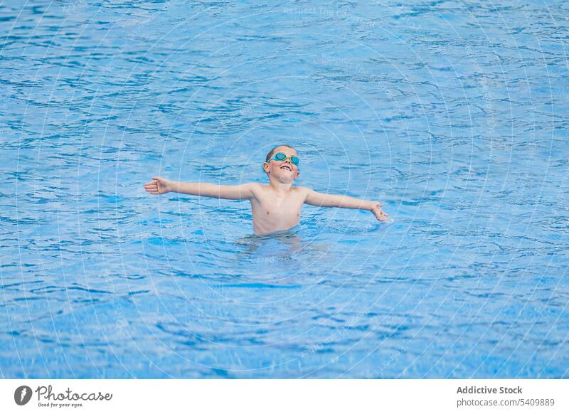 Fröhliches, süßes Kind mit Schwimmbrille, das allein im Schwimmbad steht und spielt Schutzbrille Glück froh Lächeln genießen Pool Wasser Sommer Junge